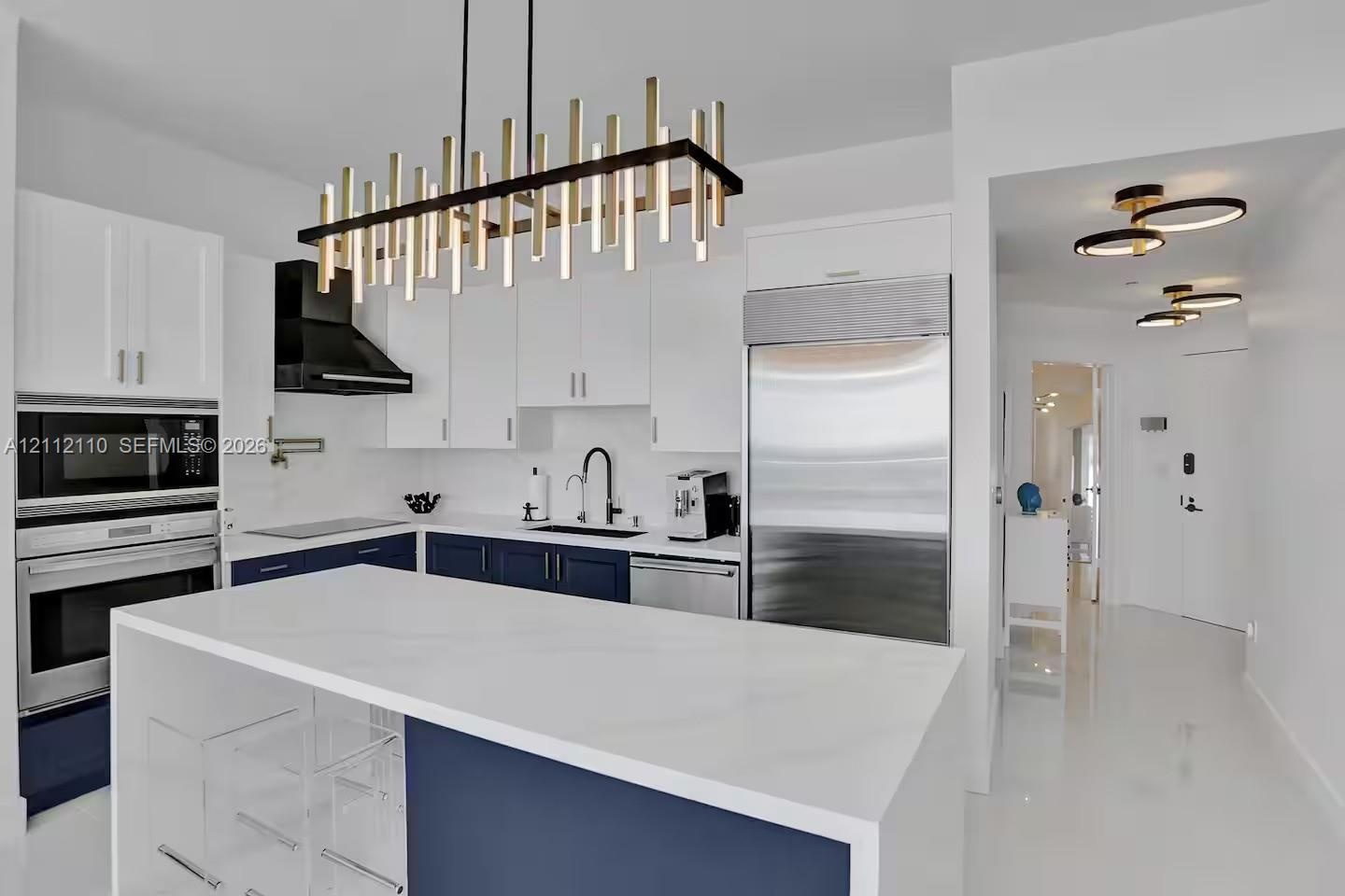 Kitchen featuring two-tone custom cabinetry, a central island with a solid-surface waterfall countertop, professional-grade stainless steel appliances