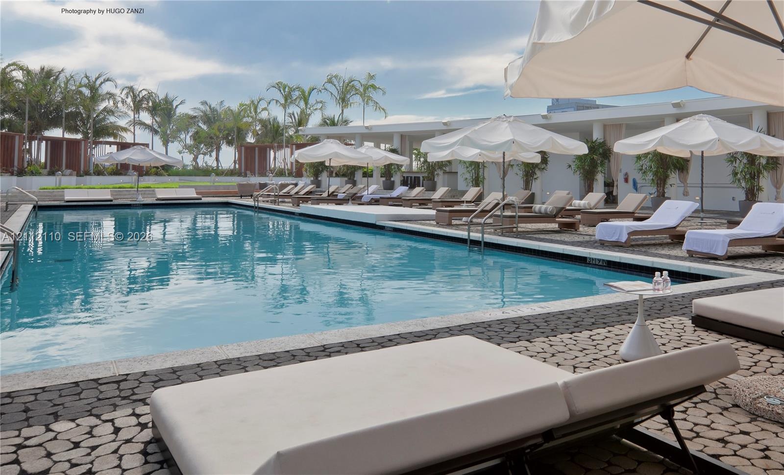Expansive rectangular swimming pool featuring a pebble-tiled deck, metal handrails, and surrounding concrete pillars