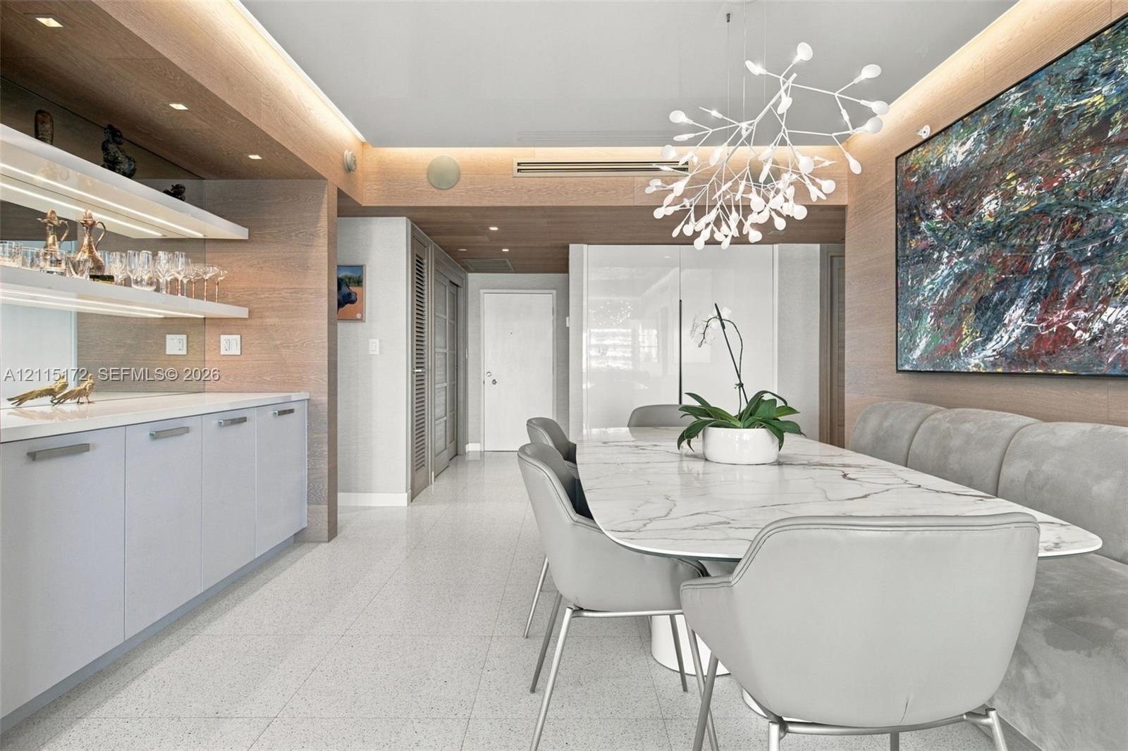 Built-in wet bar with illuminated shelving, integrated cabinetry, wood-finish wall paneling, ceiling recessed lighting, and a modern sculptural pendan