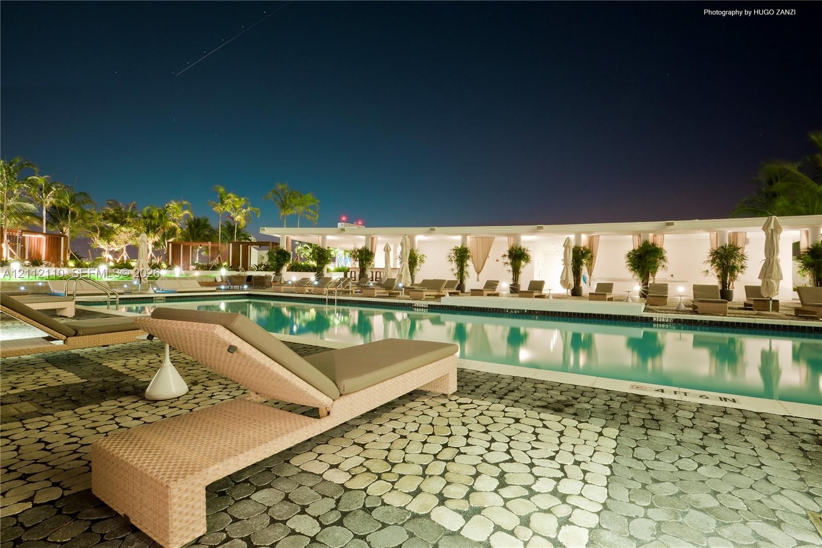 In-ground swimming pool featuring a decorative stone paver deck and a covered patio structure with built-in columns