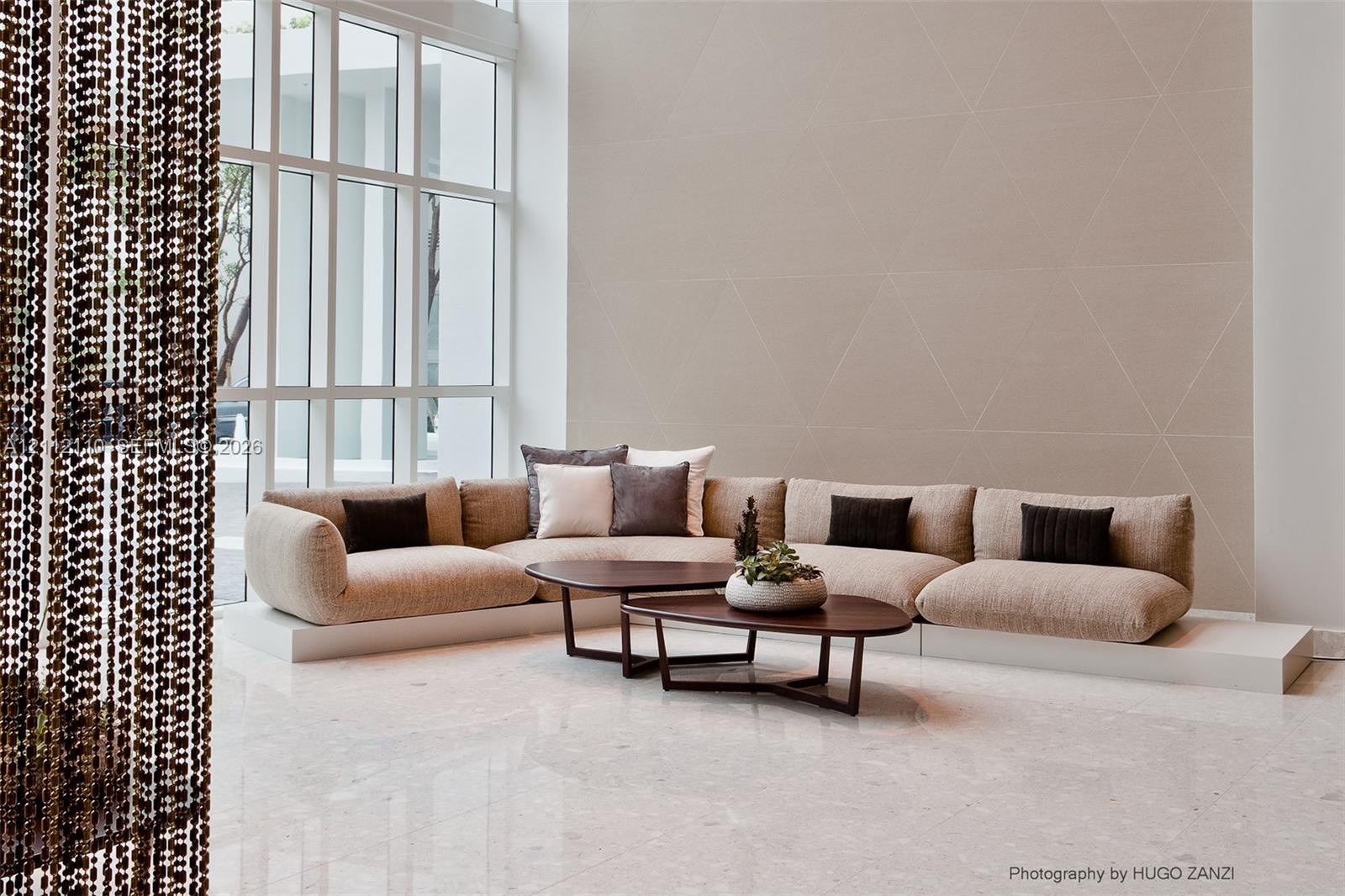 Double-height floor-to-ceiling windows, polished stone flooring, and geometric patterned accent wall