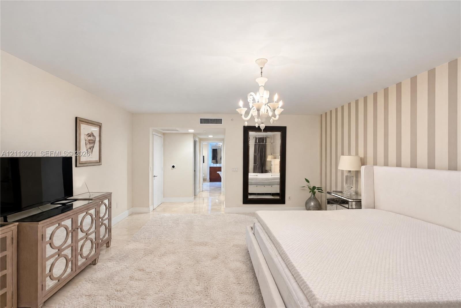 Spacious interior featuring a multi-arm crystal chandelier, wall-to-wall carpeting, and an accent wall with vertical striped wallcovering