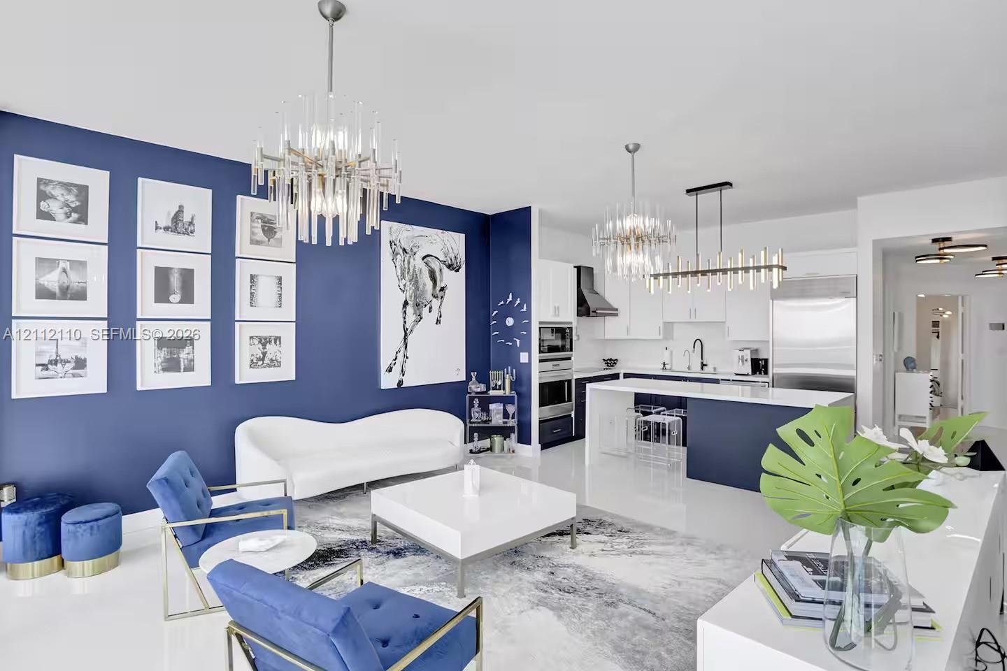 Open-concept living space featuring high-gloss flooring, tiered crystal chandeliers, two-tone custom cabinetry, a stone-topped kitchen island, and a d