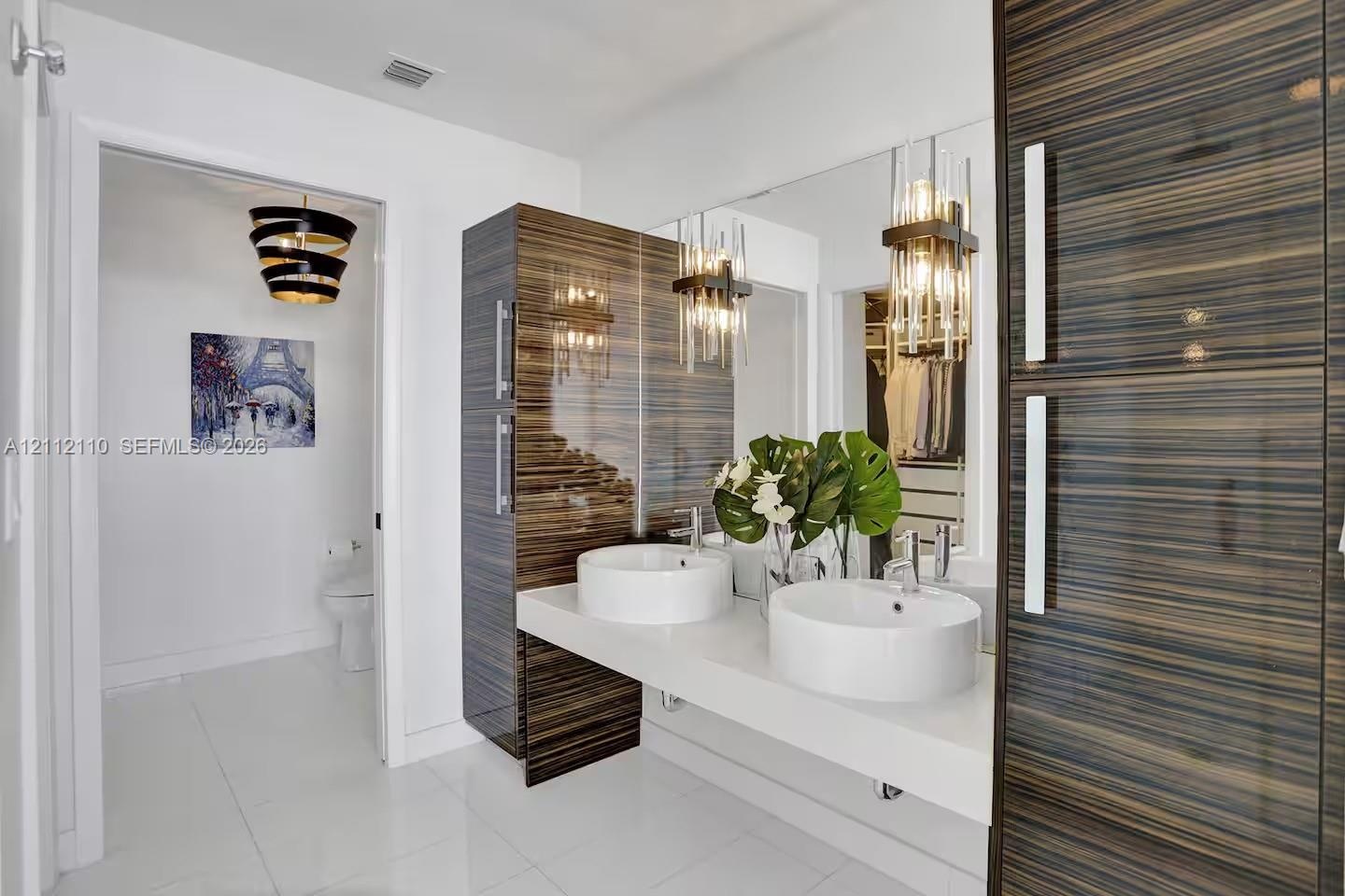 Floating vanity with dual vessel sinks, high-gloss horizontal wood-grain cabinetry, polished white surfaces, and contemporary multi-pendant lighting