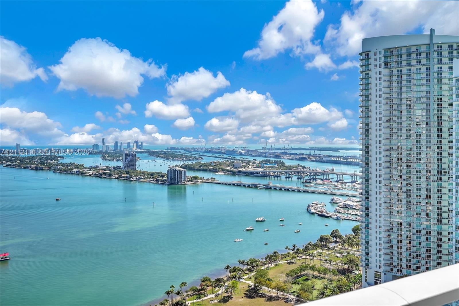 High-rise building with a prominent glass-paneled balcony railing, overlooking a coastal expanse featuring bridges, a waterway, and urban skyline scen