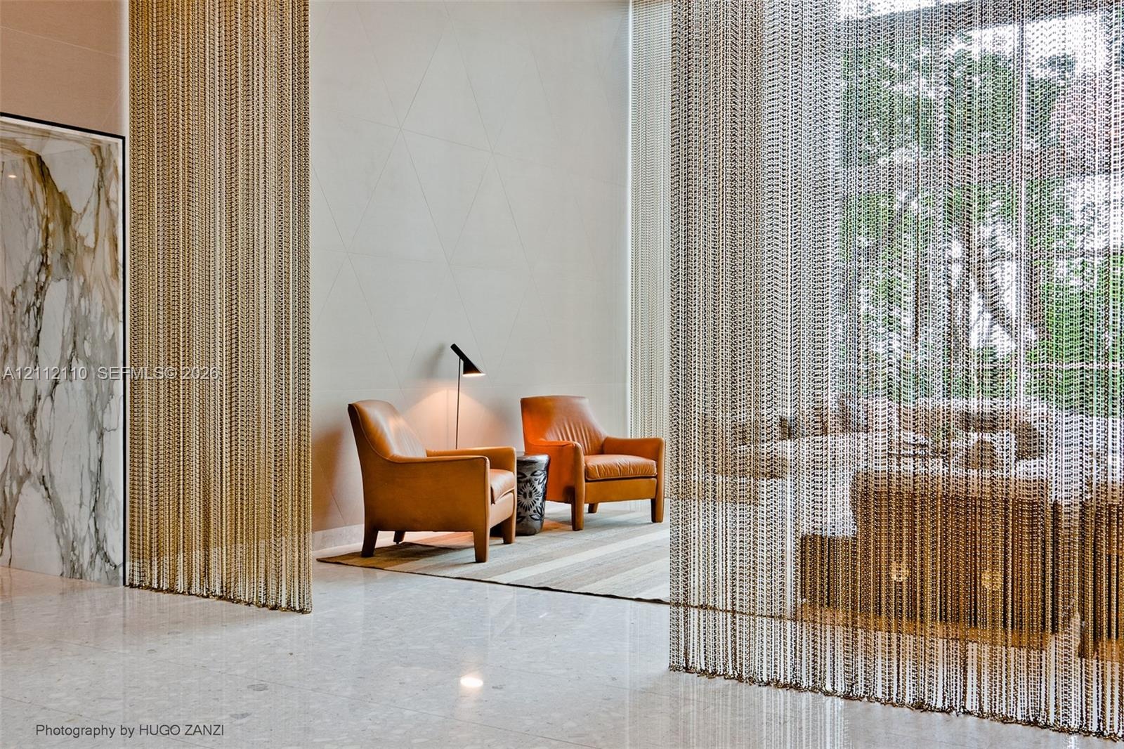 Double-height space featuring floor-to-ceiling metal chain drapery, high-gloss stone flooring, floor-to-ceiling stone wall paneling, and geometric tex
