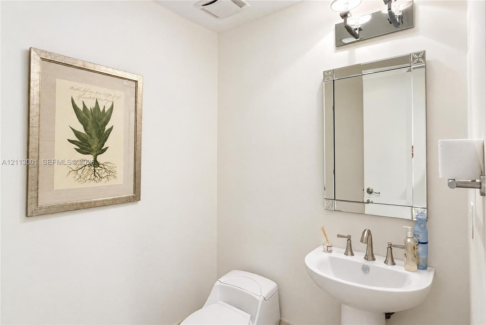 Powder room featuring a wall-mounted pedestal sink with a metallic widespread faucet, a rectangular beveled-edge wall mirror, and overhead decorative 