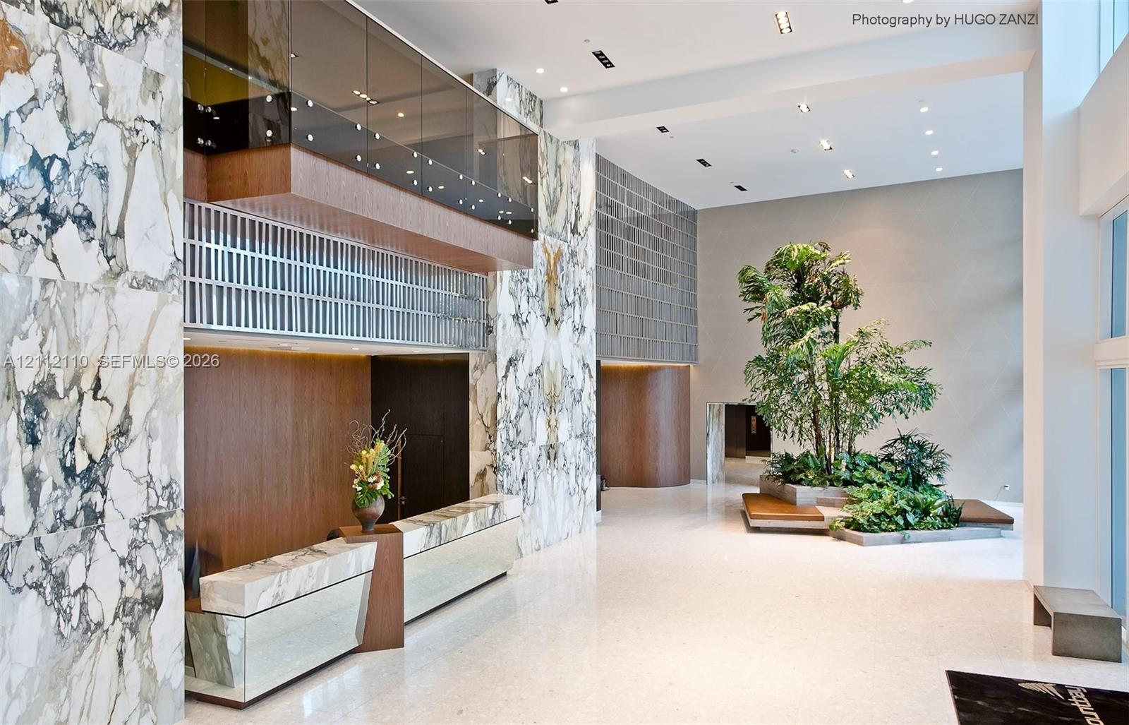 Grand foyer featuring floor-to-ceiling stone wall cladding, polished stone flooring, recessed ceiling lighting, a built-in stone reception desk, and a