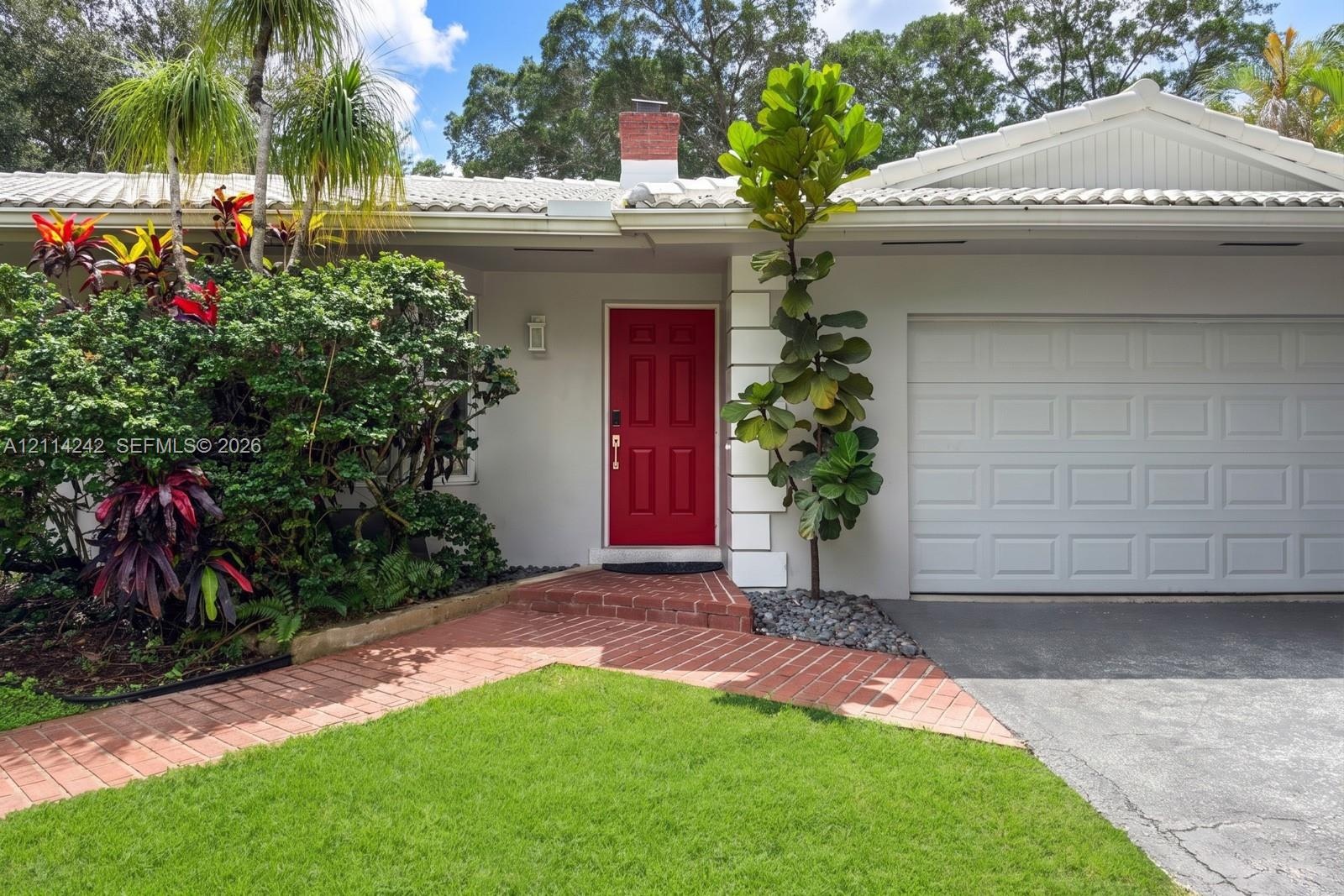 Single-story exterior featuring a brick walkway, tiled roof, chimney, and attached garage