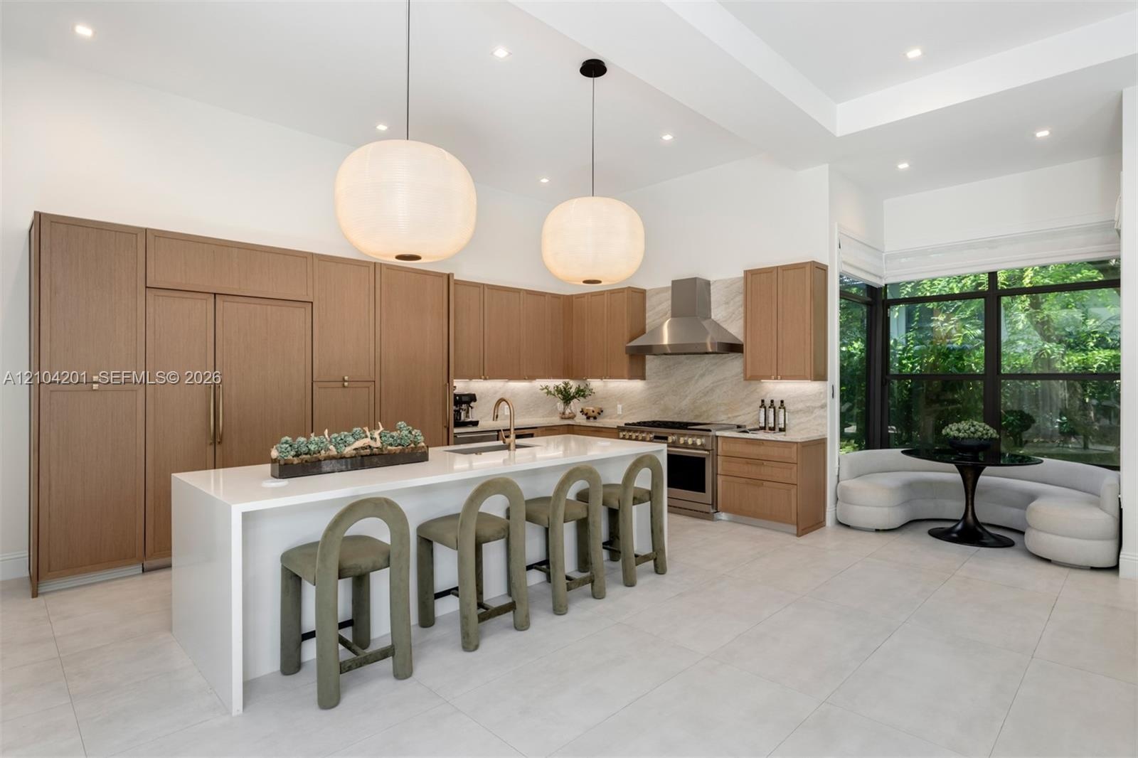 Kitchen featuring flat-panel wood cabinetry, large waterfall-edge island, stone-surround range hood, integrated stainless steel appliances, and large-