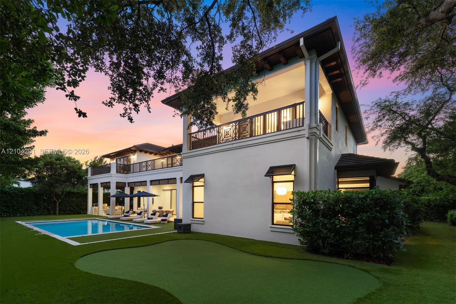 Two-story stucco exterior featuring a tiered roofline, expansive covered balconies with patterned railings, an integrated putting green, and a rectang