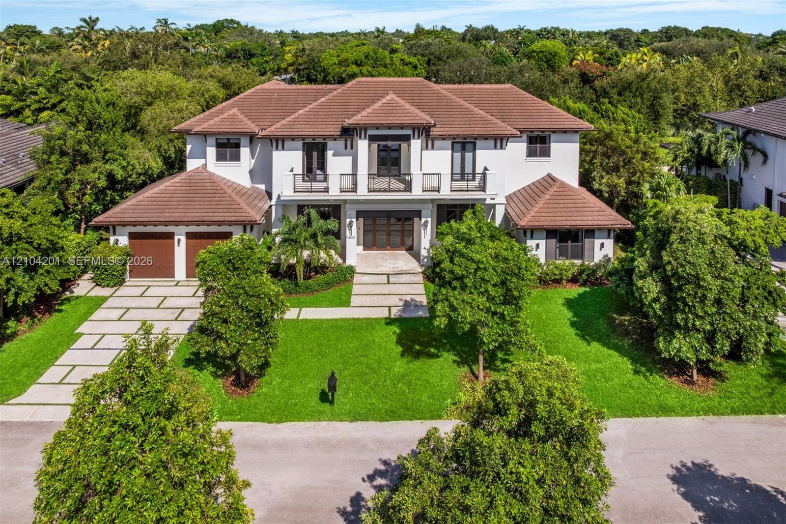 Two-story stucco exterior featuring a multi-hipped tile roof, balcony with decorative metal railings, paver driveway, and multiple double-door entries