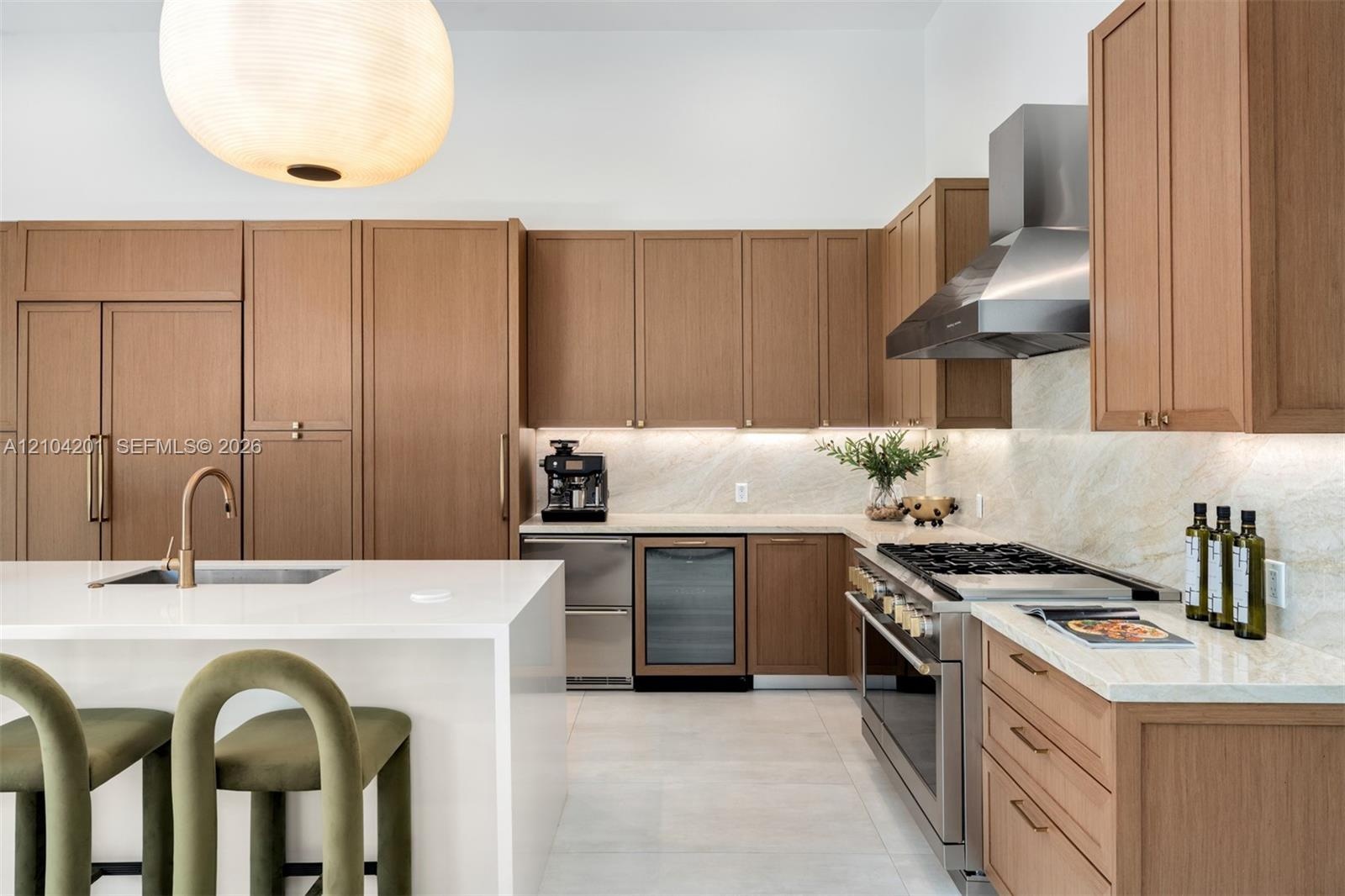 Kitchen featuring wood cabinetry, white stone countertops, integrated stainless steel appliances, a stainless steel range hood, and a large central is