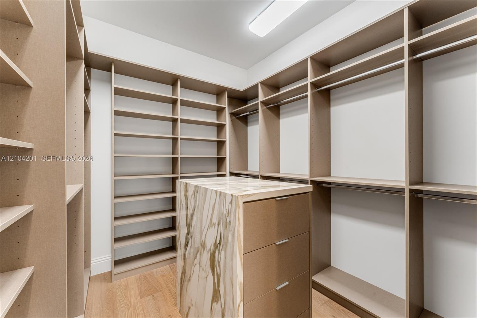 Custom walk-in closet featuring extensive built-in shelving, integrated hanging rods, a central island with a stone-finish countertop, and three built