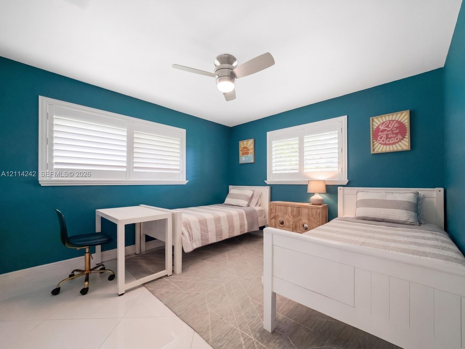 Bedroom featuring white plantation shutters, polished tile flooring, and a ceiling-mounted light and fan fixture