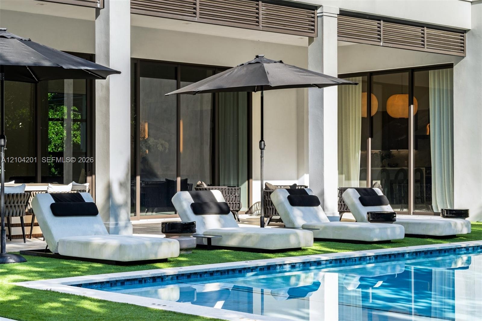 Covered patio featuring structural columns, decorative louvered detailing, sliding glass doors, and a swimming pool with tile edging