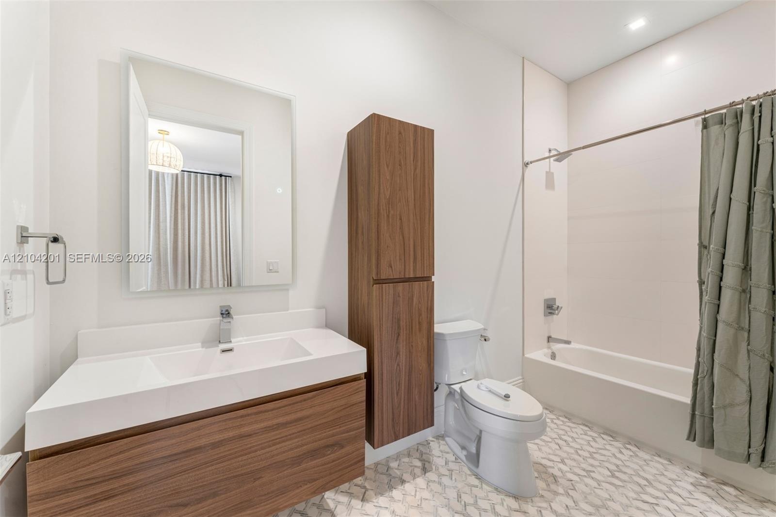 Floating vanity with wood-finish cabinetry, rectangular integrated sink, tall linen storage cabinet, and patterned tile flooring