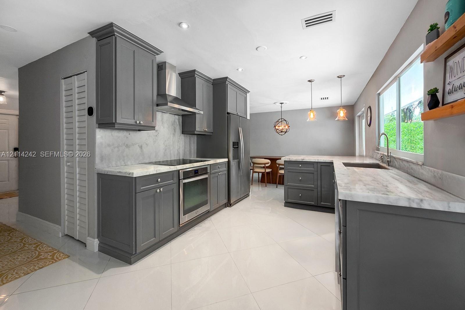 Kitchen featuring dark grey shaker-style cabinetry, stone-finish countertops with matching backsplash, stainless steel appliances including a chimney-