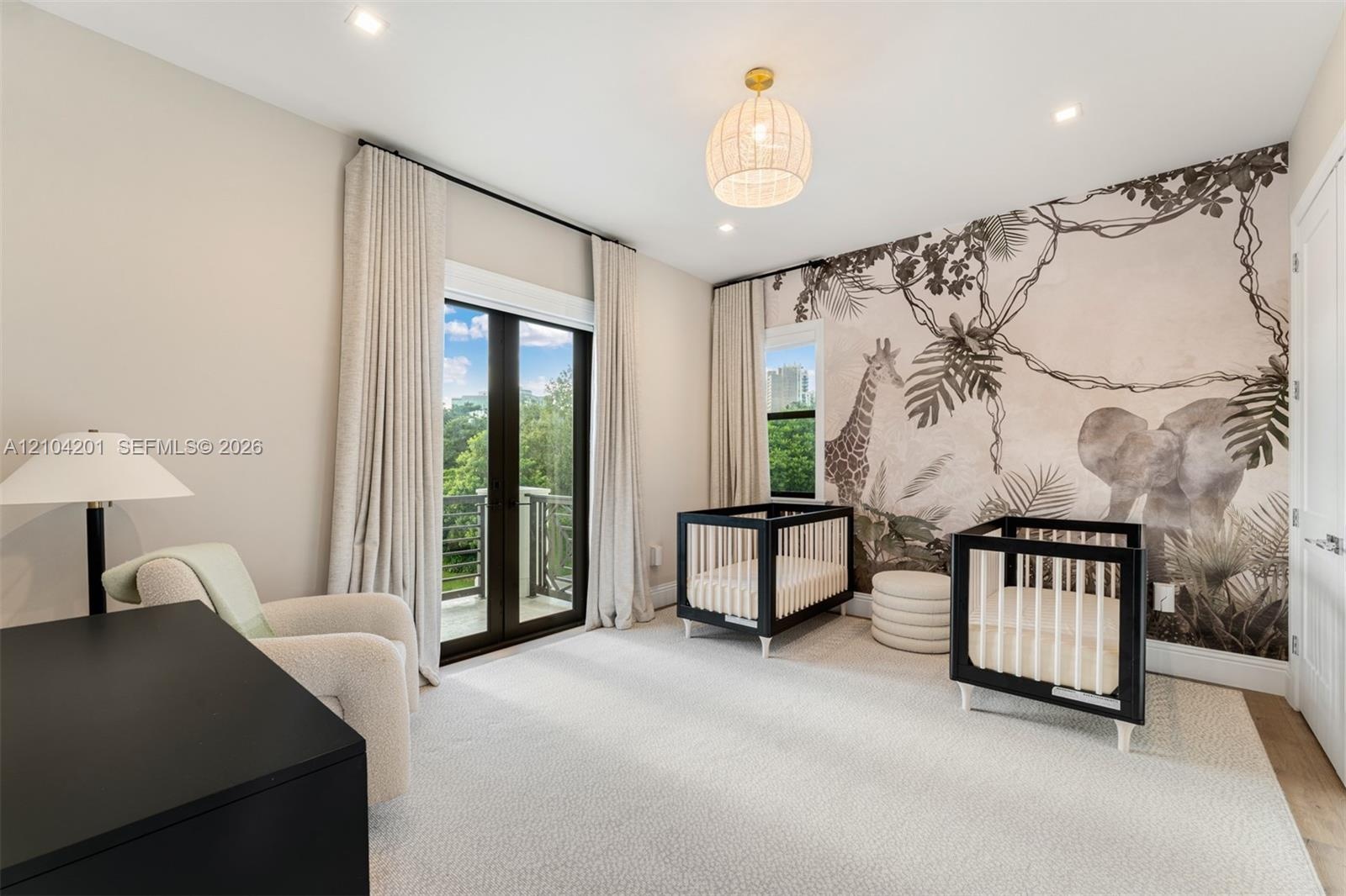 Neutral carpeted flooring, full-wall decorative mural, recessed lighting, brass-toned pendant fixture, and double glass doors providing outdoor access