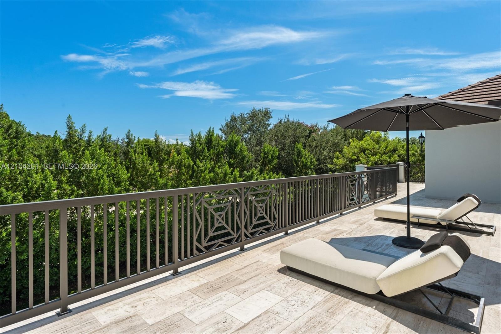 Stone-tiled balcony featuring a decorative metal railing with geometric inlay, overlooking mature tree-lined scenery