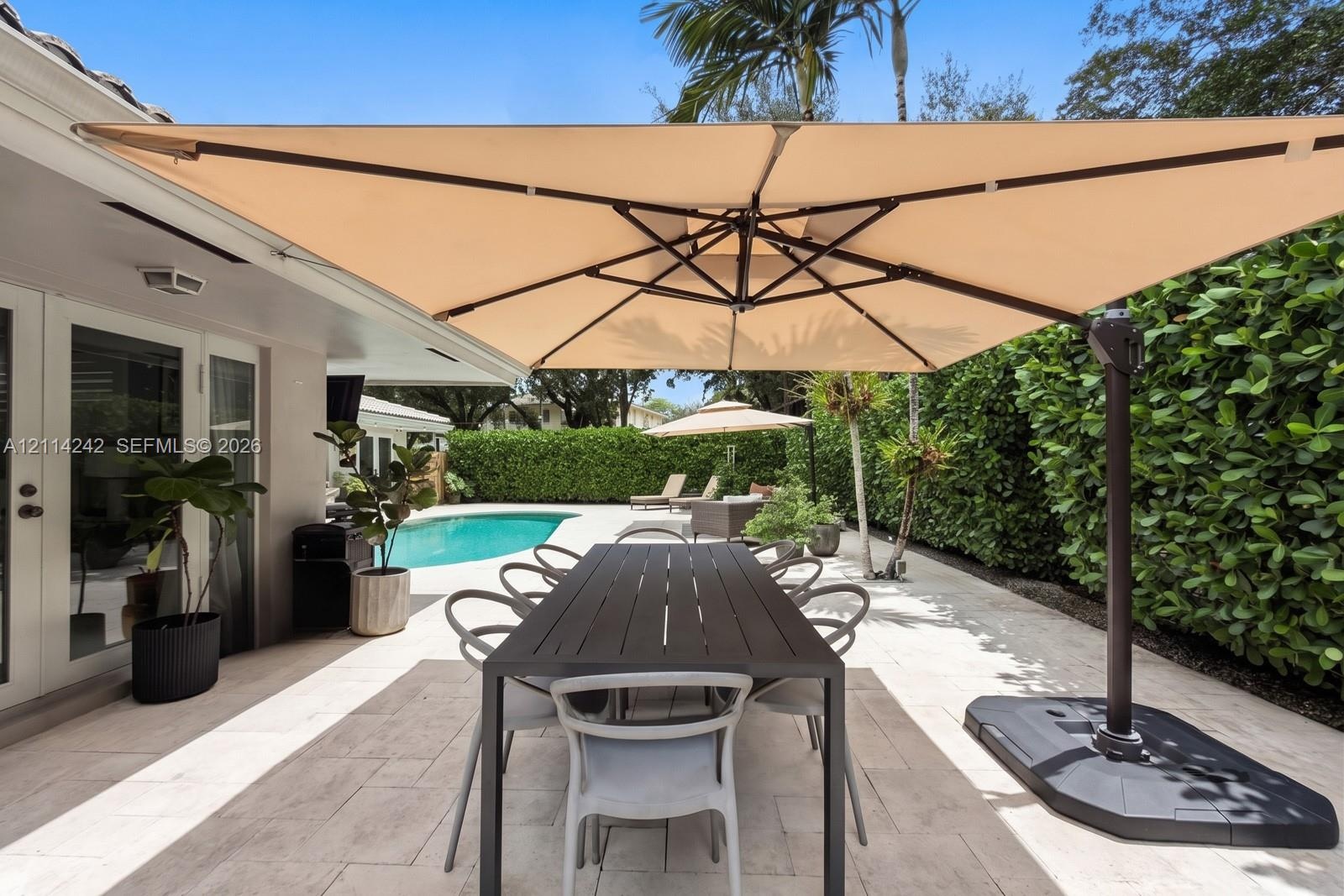 Covered stone patio featuring a swimming pool, integrated landscaping, and French doors