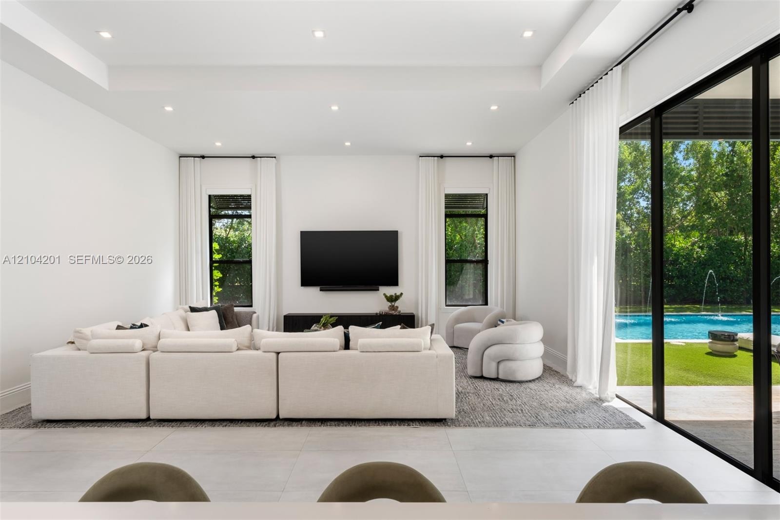 Tray ceiling with recessed lighting, large-format tile flooring, and floor-to-ceiling glass sliding doors opening to an exterior swimming pool and pat