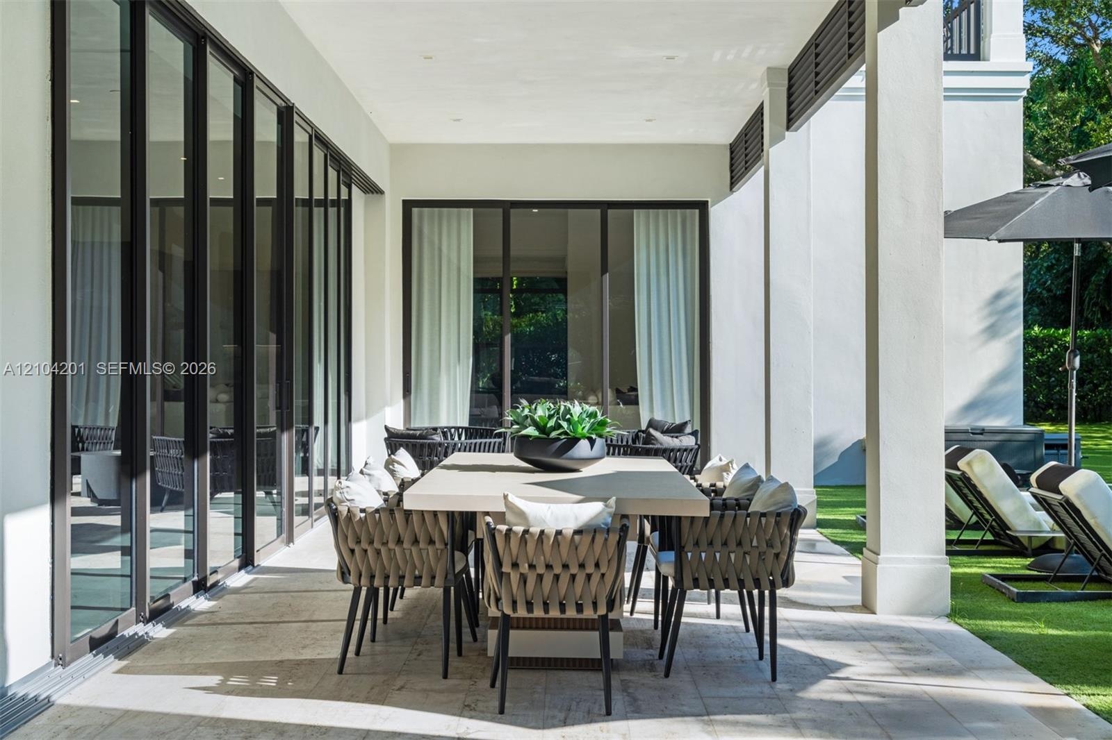 Covered patio featuring stone-tile flooring, floor-to-ceiling glass panel doors with dark frames, and structural square columns