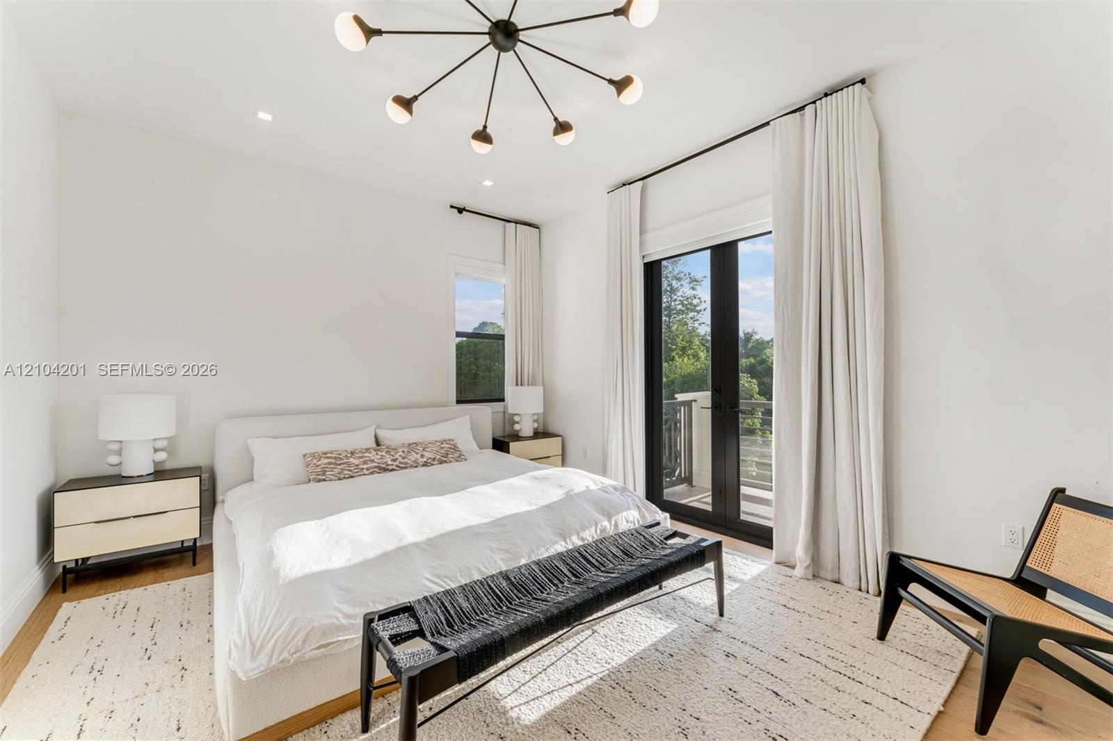Modern bedroom featuring recessed lighting, a multi-arm sputnik chandelier, wood-finish flooring, and black-framed French doors opening to an exterior