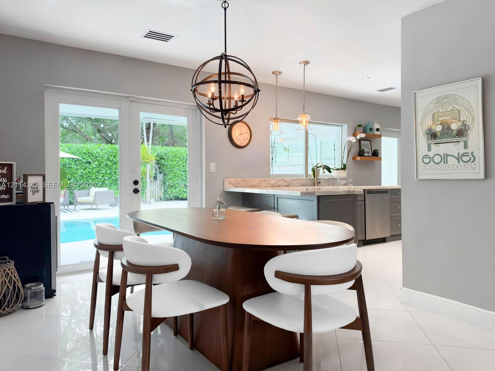 Orbital metal chandelier, solid-surface breakfast bar, stainless steel dishwasher, glass French doors, and porcelain tile flooring