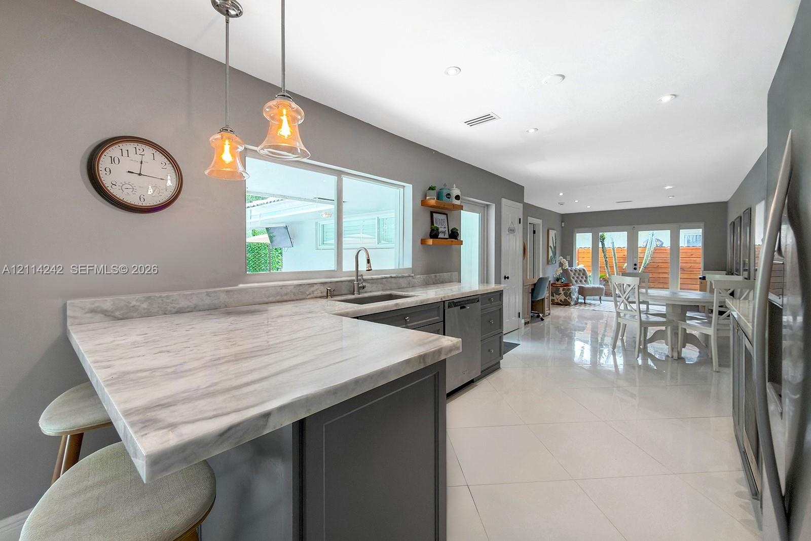 Kitchen featuring stone-finish countertops with an integrated breakfast bar, dark-tone cabinetry, stainless steel dishwasher, dual pendant lighting, a