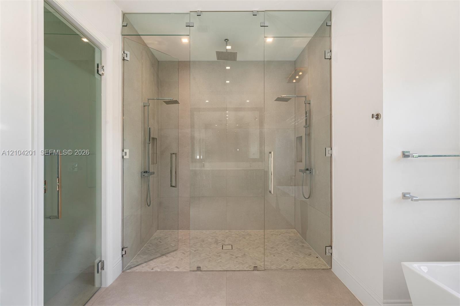Walk-in shower featuring large-format stone-tile walls, glass-enclosed entry, dual rainfall showerheads, handheld sprayers, and textured stone-tile fl