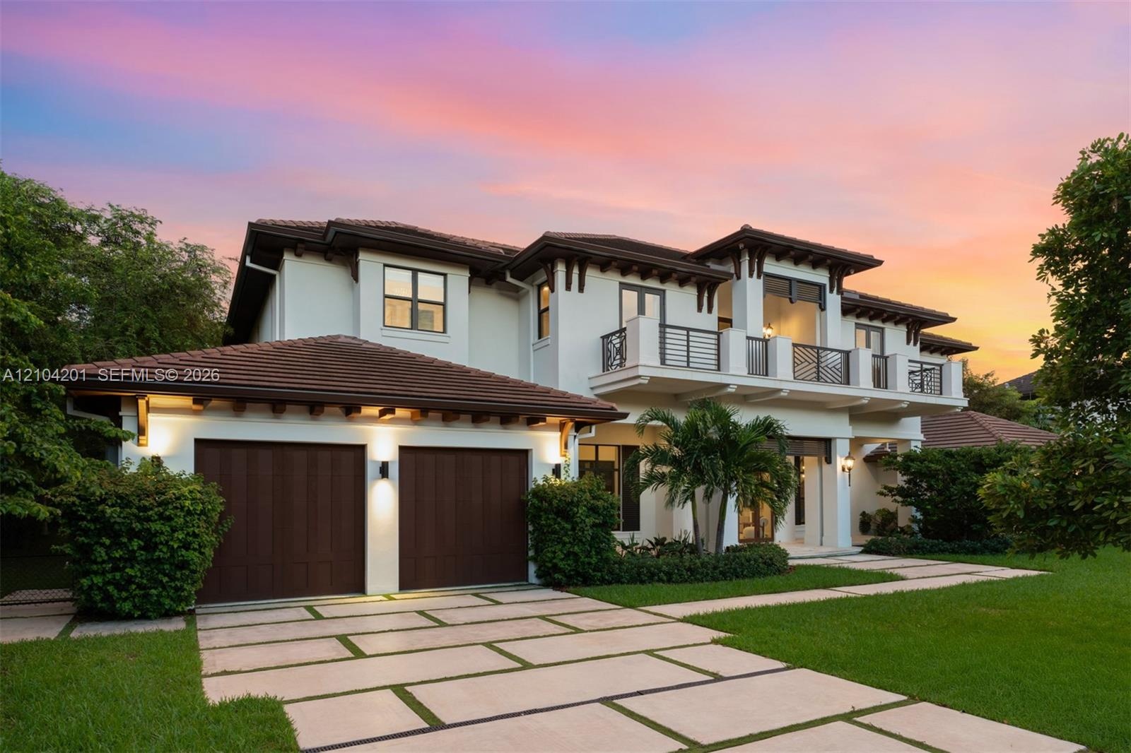 Two-story exterior featuring a tile roof, stucco finish, expansive second-story balcony with metal railings, and a multi-car garage with wood-finish d