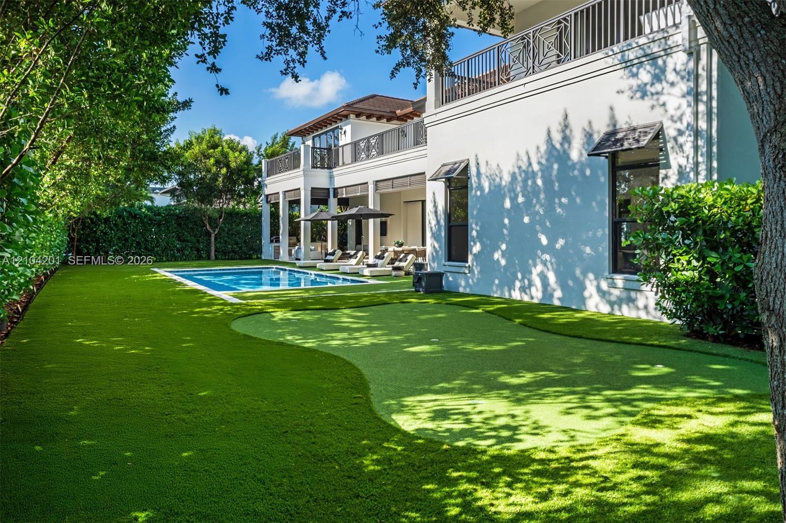 Outdoor area featuring an in-ground swimming pool, synthetic putting green, covered loggia, and second-story balcony with decorative metal railing