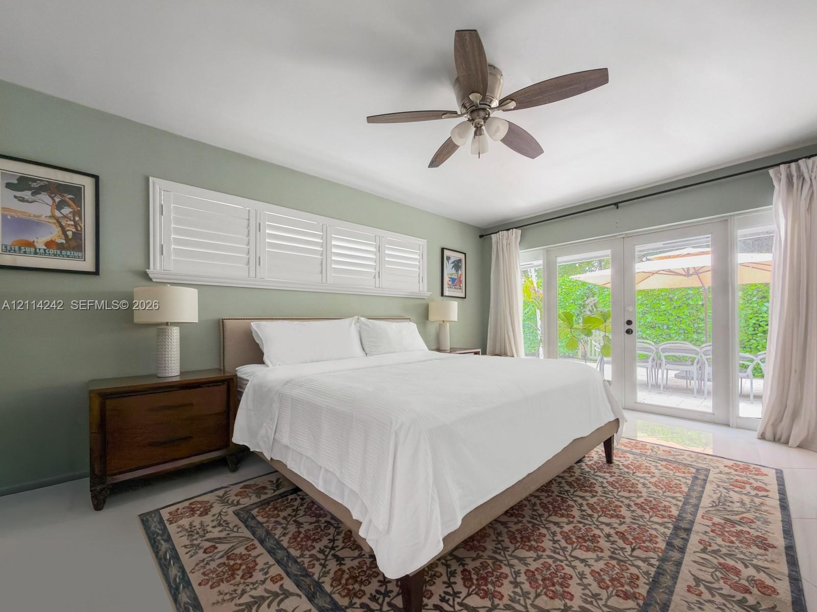 Bedroom featuring a ceiling fan with integrated lighting, plantation shutters, and glass-paned doors with exterior access