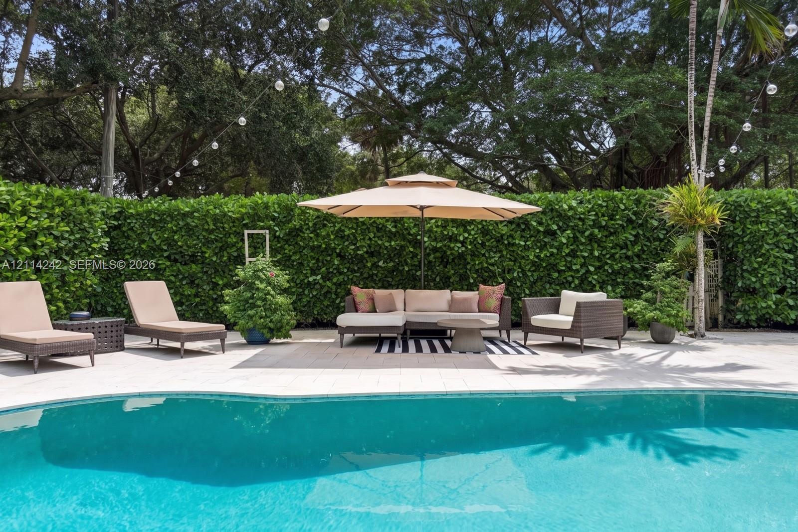 Swimming pool with stone paver decking and high hedge perimeter fencing