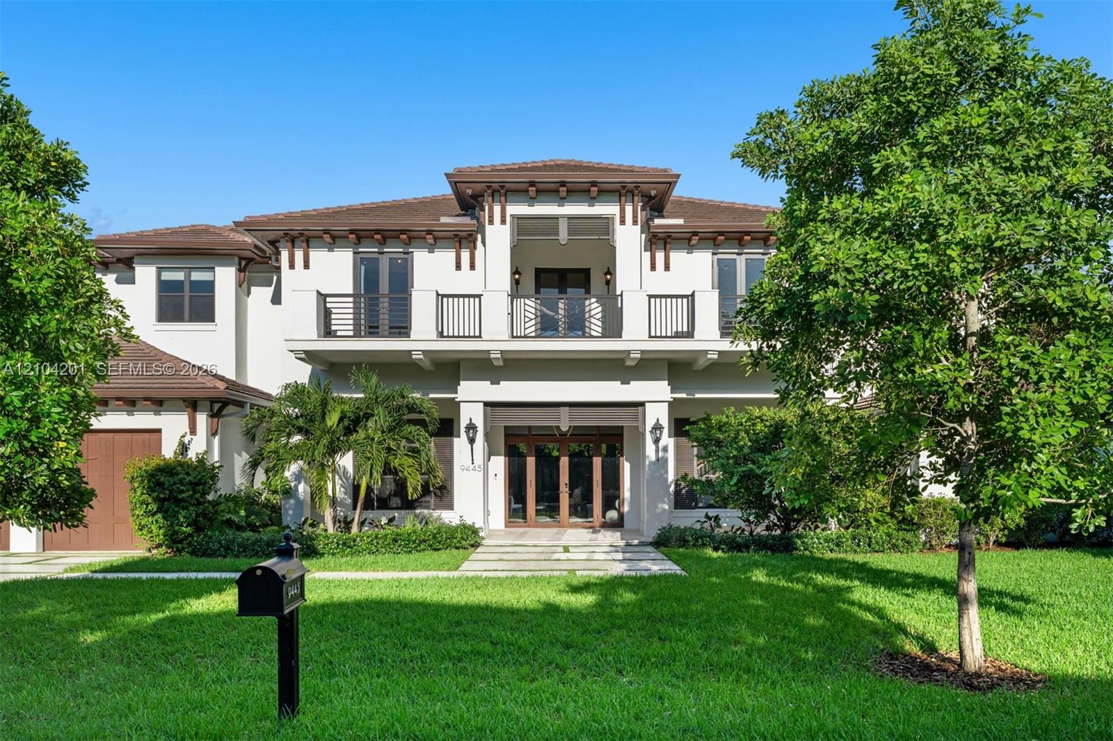 Two-story stucco exterior featuring a tiled hip roof, decorative timber rafter tails, a second-story balcony with metal railings, and a grand entrance