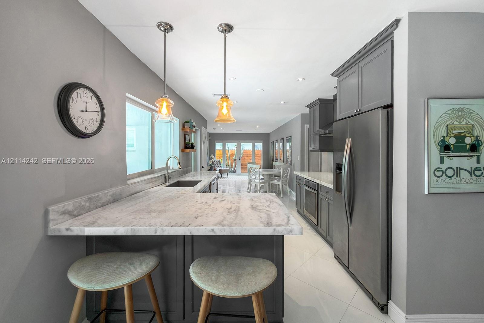 Kitchen featuring charcoal-toned cabinetry, light-toned stone-finish countertops, stainless steel appliances, polished tile flooring, and dual glass p