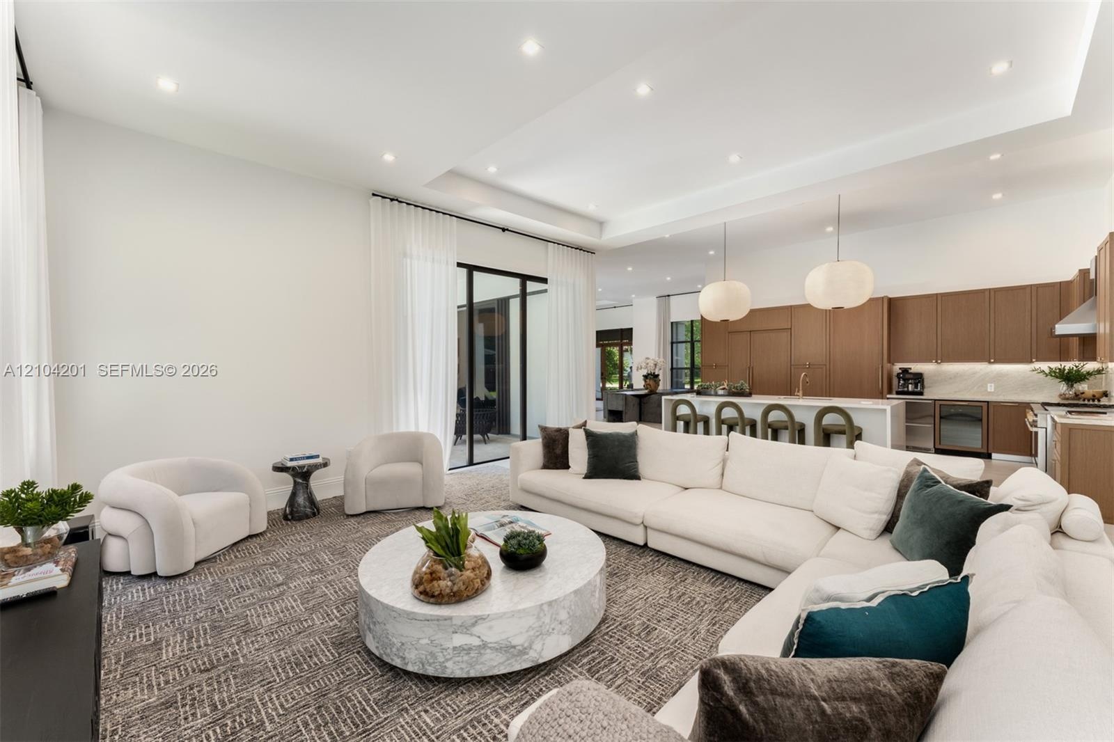 Open-concept space featuring a tray ceiling with recessed lighting, oversized glass panel doors, wood-finish cabinetry, a large kitchen island with st