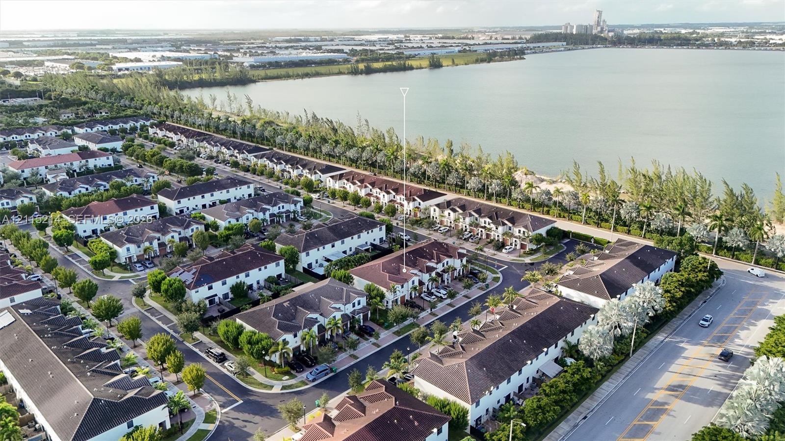 Aerial perspective of a multi-unit residential community featuring clay tile roofing, paved streets, and direct proximity to a large water body