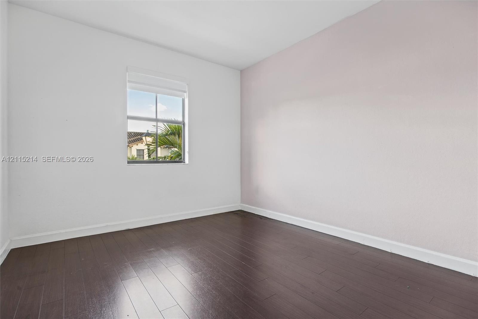 Room featuring dark wood-finish flooring, a single window, and a light-toned accent wall