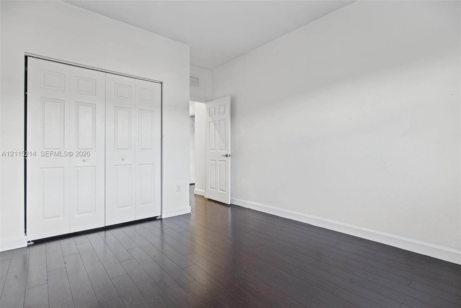 Interior space featuring dark wood-finish flooring, white walls, and a white six-panel bifold closet door