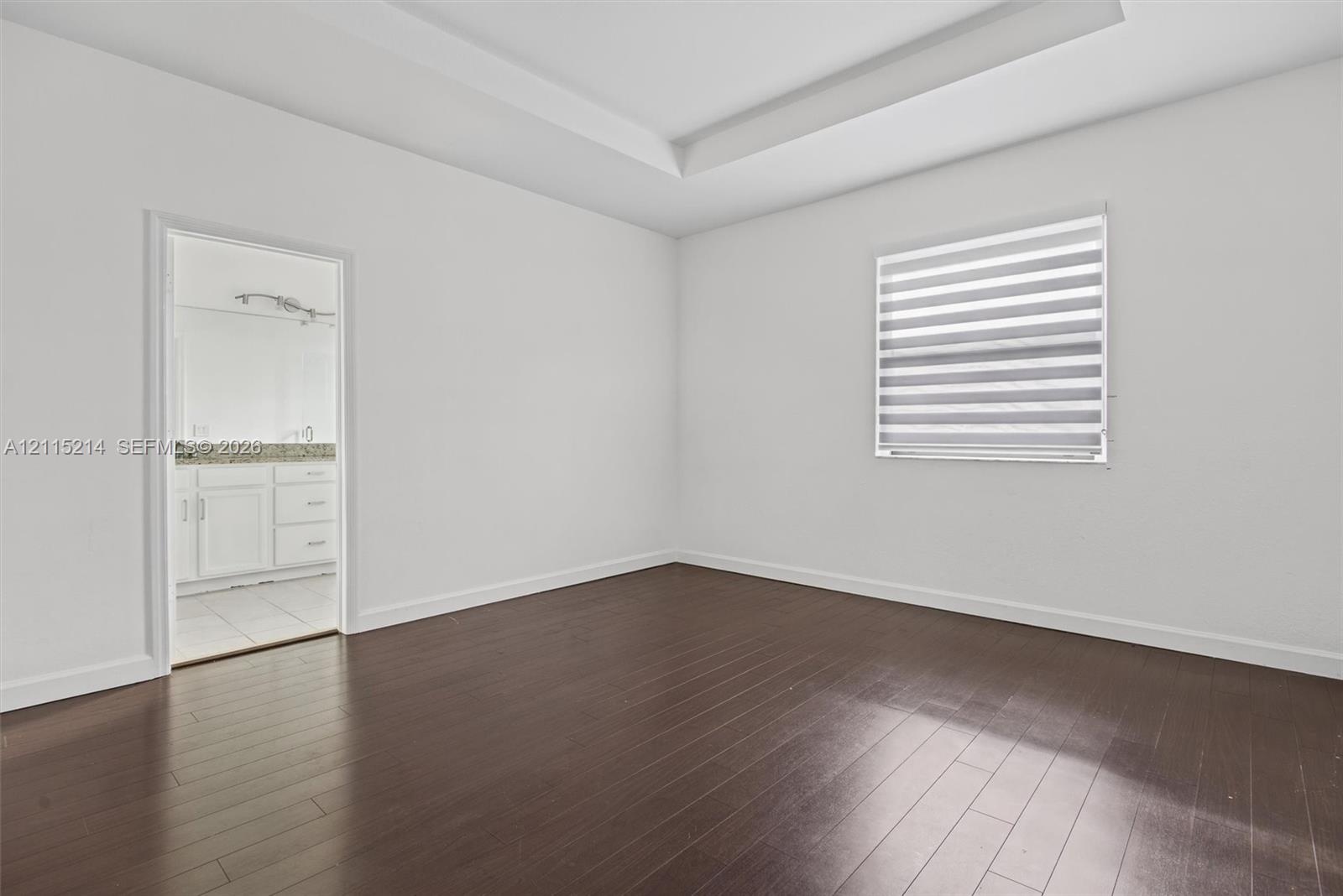 Room featuring tray ceilings, wood-finish flooring, and horizontal banded window shades