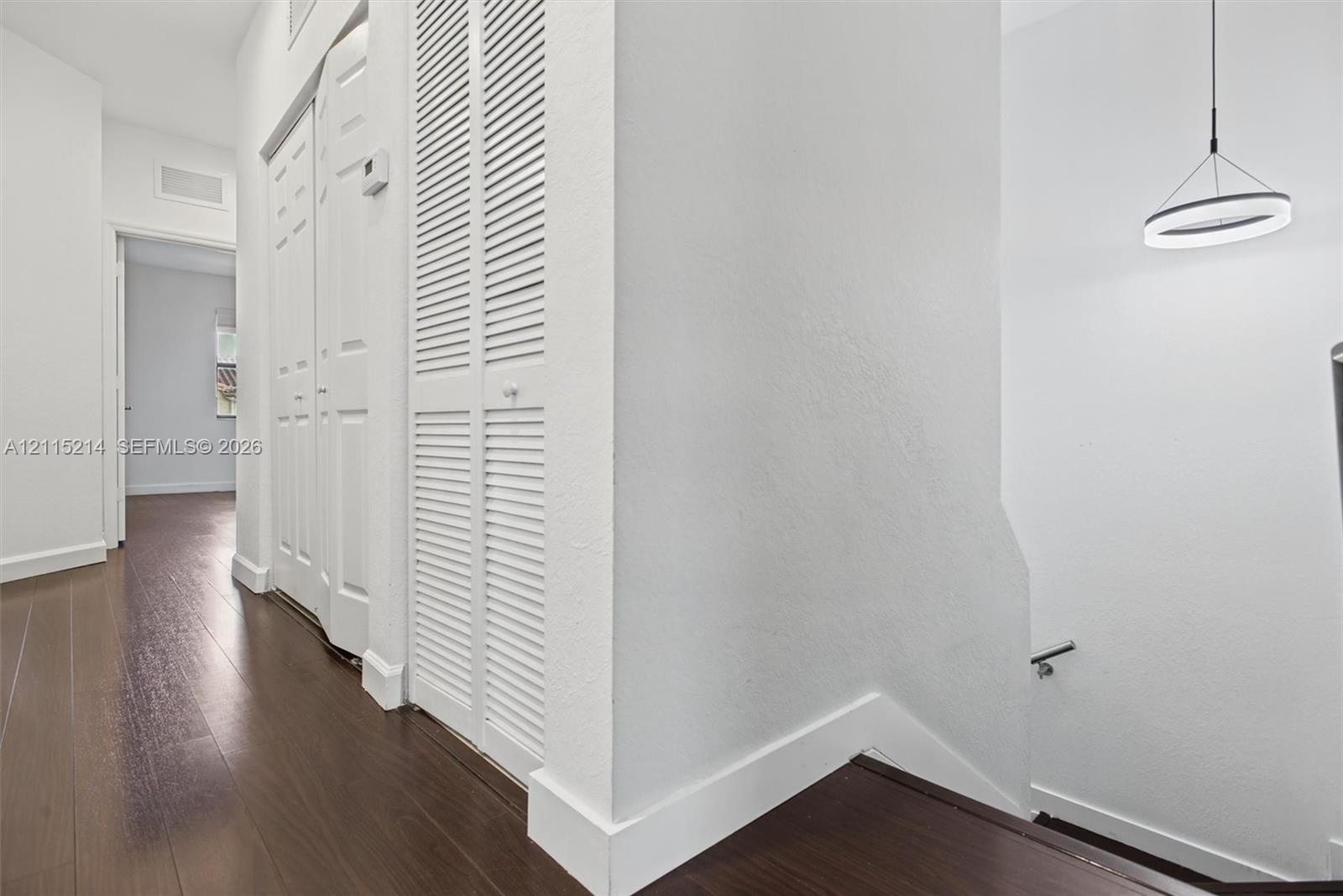 Interior hall featuring wood-finish flooring, white louvered-door closets, and a circular LED pendant light fixture