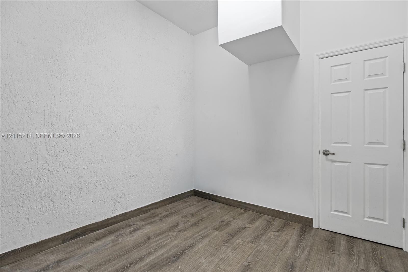Interior space featuring textured walls, wood-finish flooring, and a six-panel door with brushed metal hardware