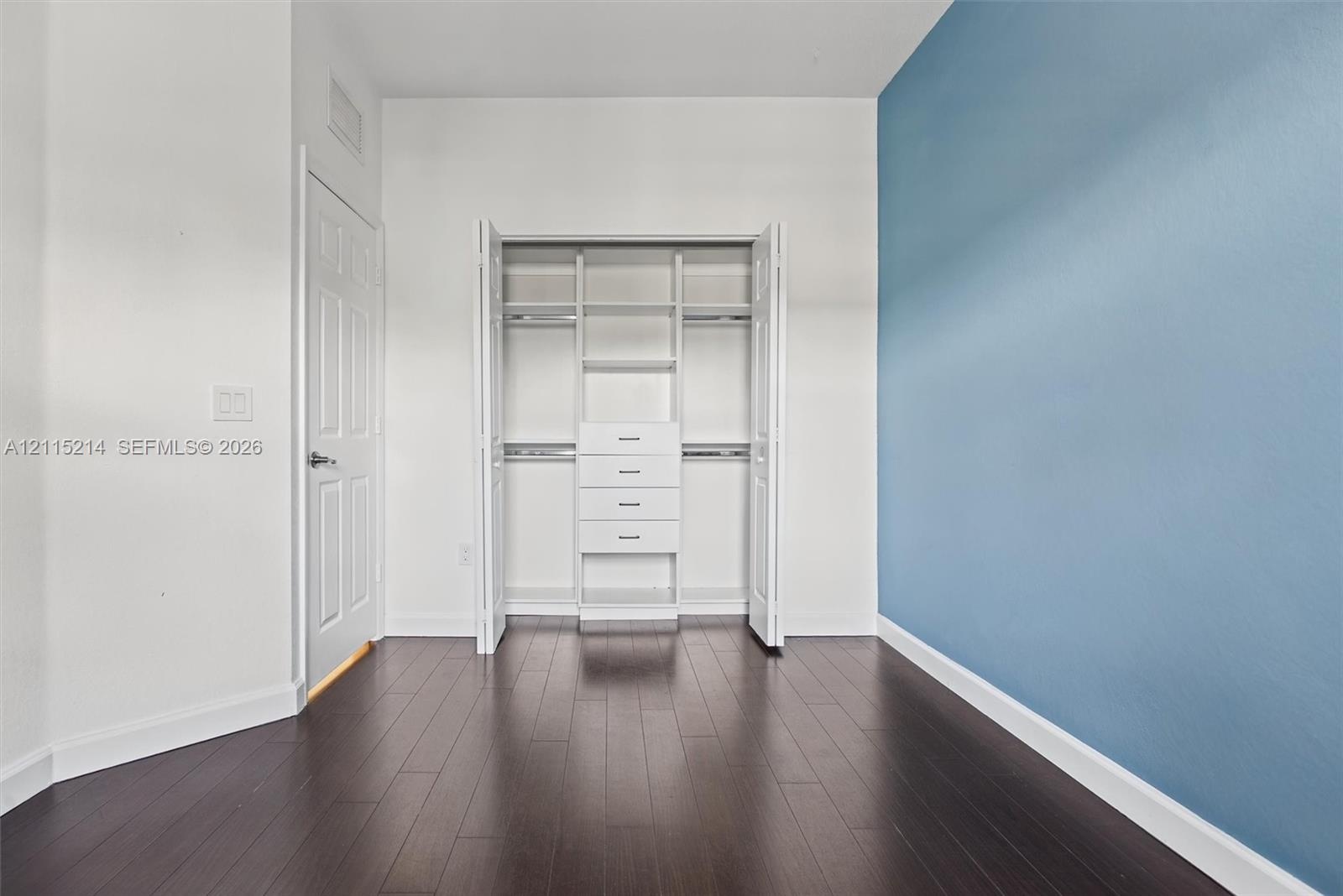 Dark wood-finish flooring, accent wall, and custom built-in closet organization featuring dual hanging rods and center storage drawers