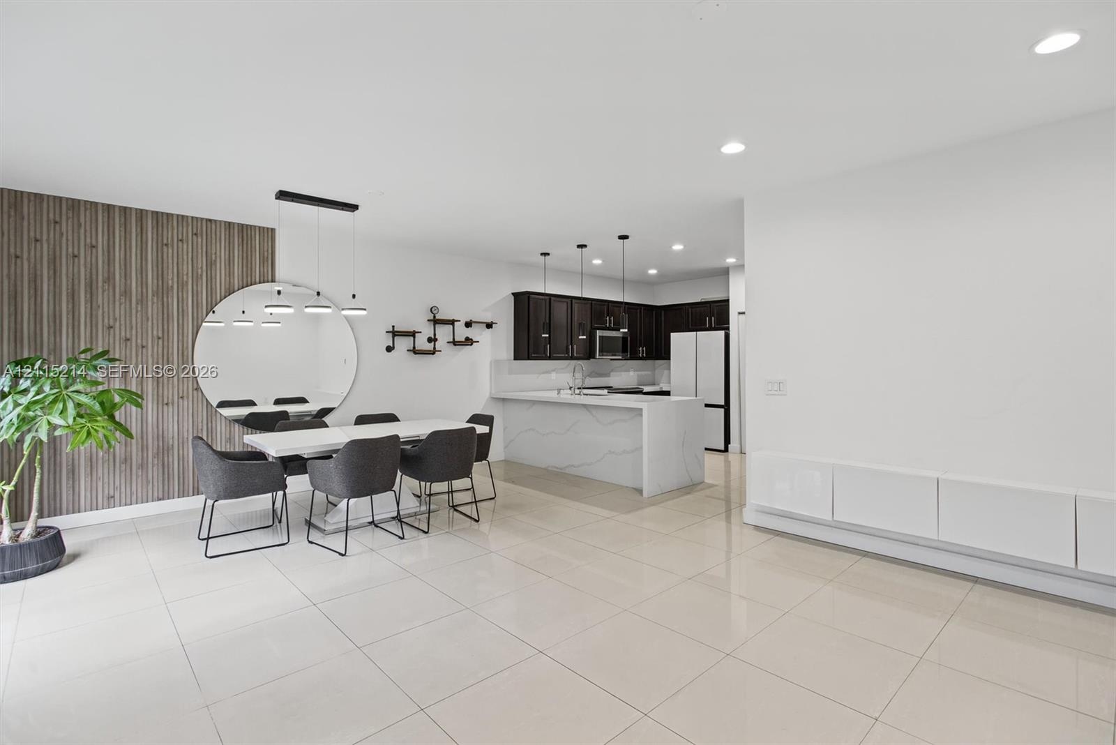 Open-concept area featuring oversized neutral floor tiling, a vertical wood-slat accent wall, recessed lighting, and a kitchen equipped with dark cabi