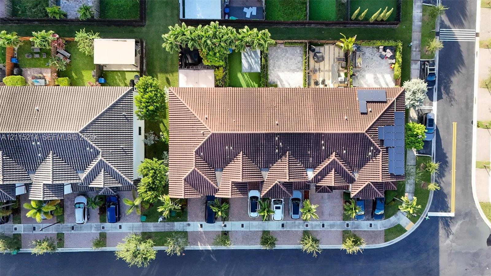 Aerial perspective featuring a multi-unit residential structure with a hipped tile roof, integrated solar panels, private paver driveways, and landsca