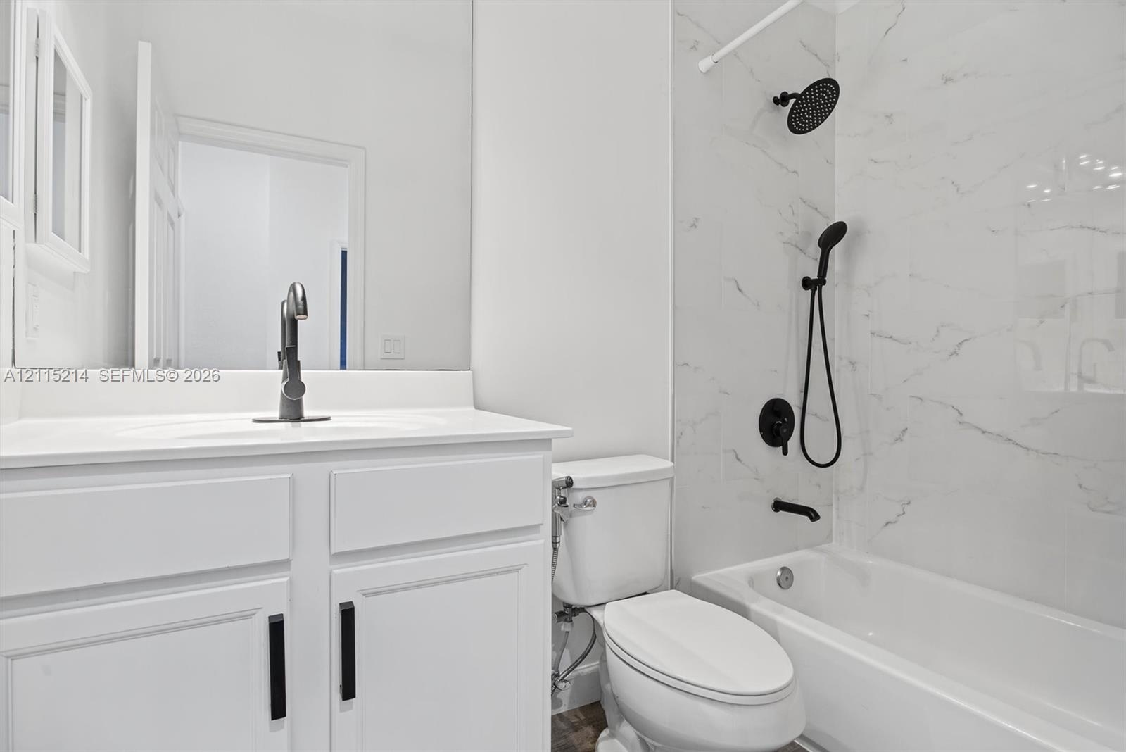 Bathroom featuring a white vanity cabinet with a solid surface countertop, matte black hardware, dual shower heads, and full-height stone-finish wall 