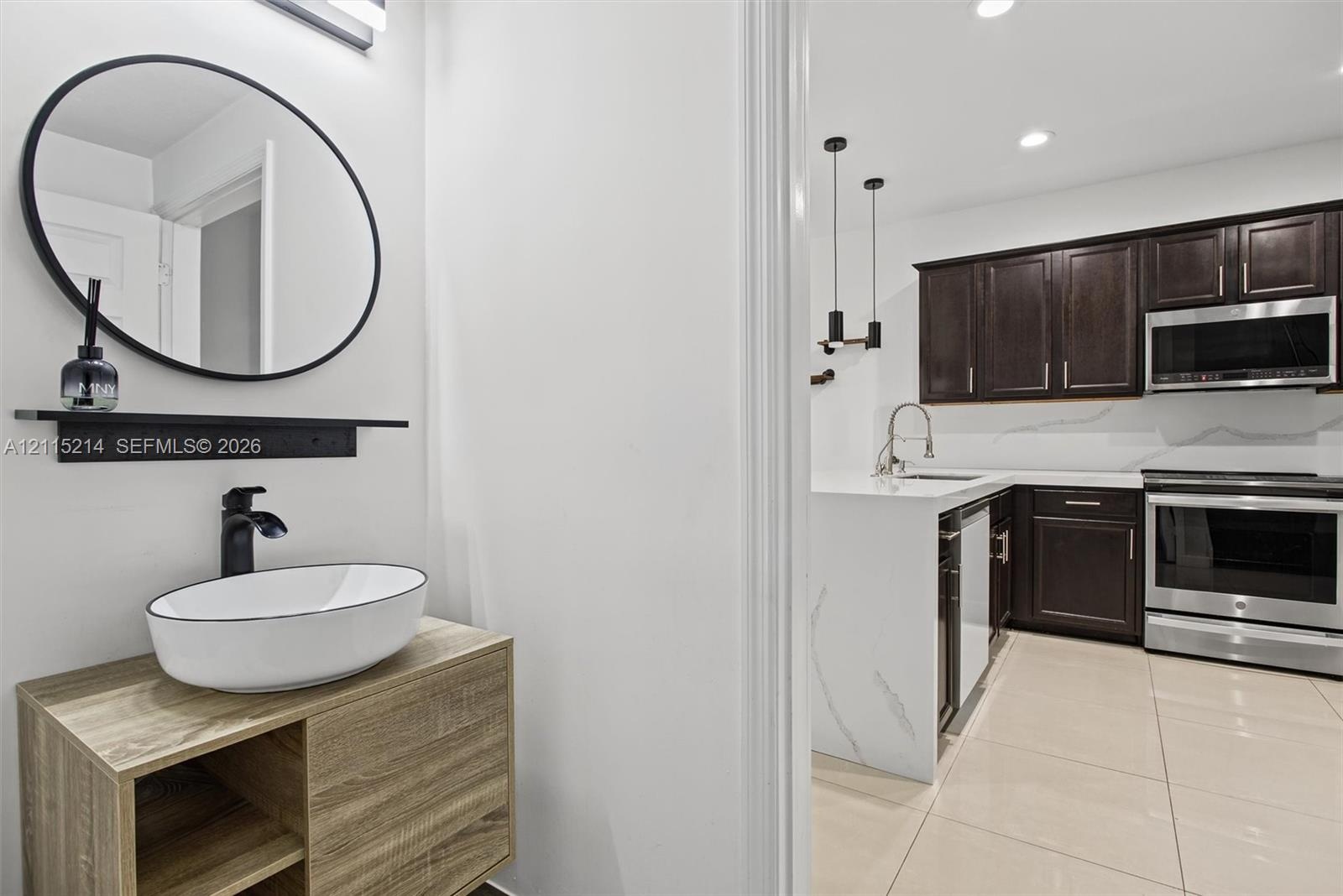 Powder room featuring a wood-finish floating vanity with a white vessel sink and matte black faucet, accented by a circular wall-mounted mirror