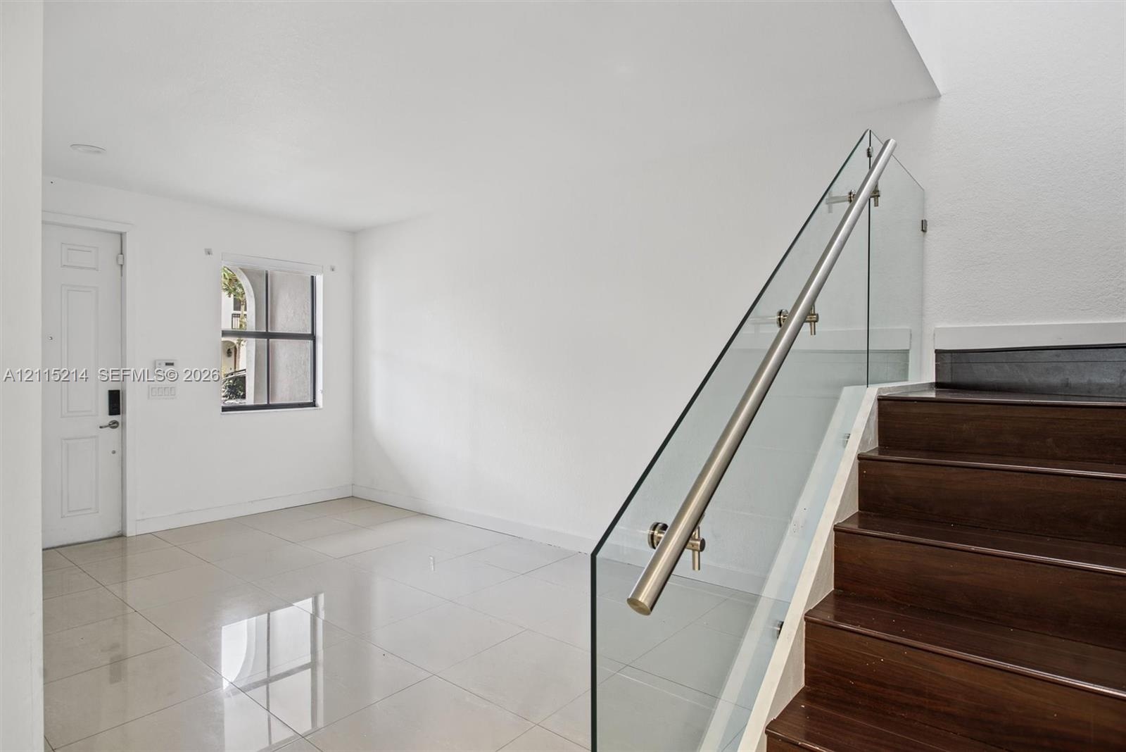 Staircase featuring dark wood-finish treads and a frameless glass railing with a metallic handrail, complemented by large-format tile flooring
